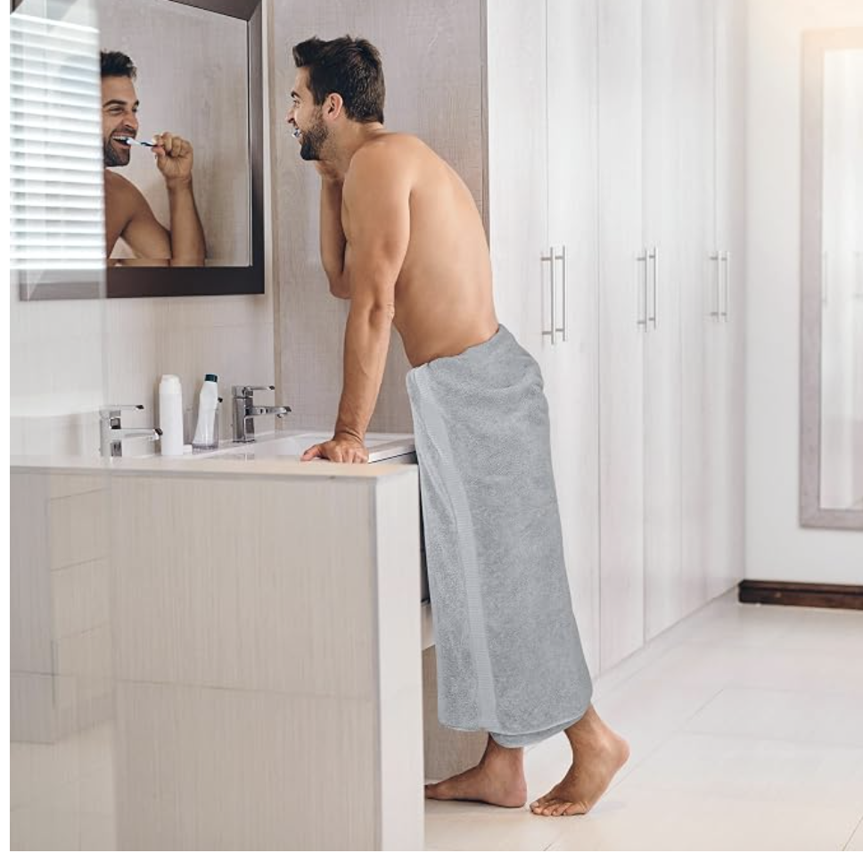 A man drying off at the bathroom sink wrapped in a grey bath towel